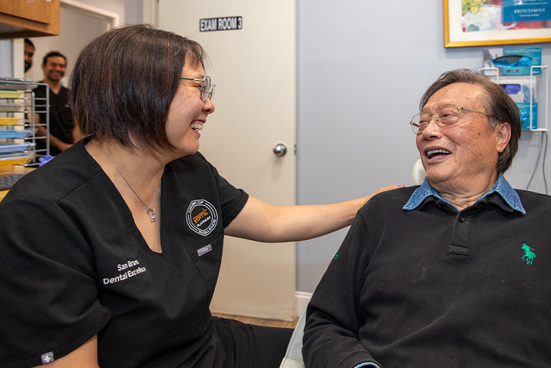 doctor with patient smiling in a dental chair with her hand on his shoulder